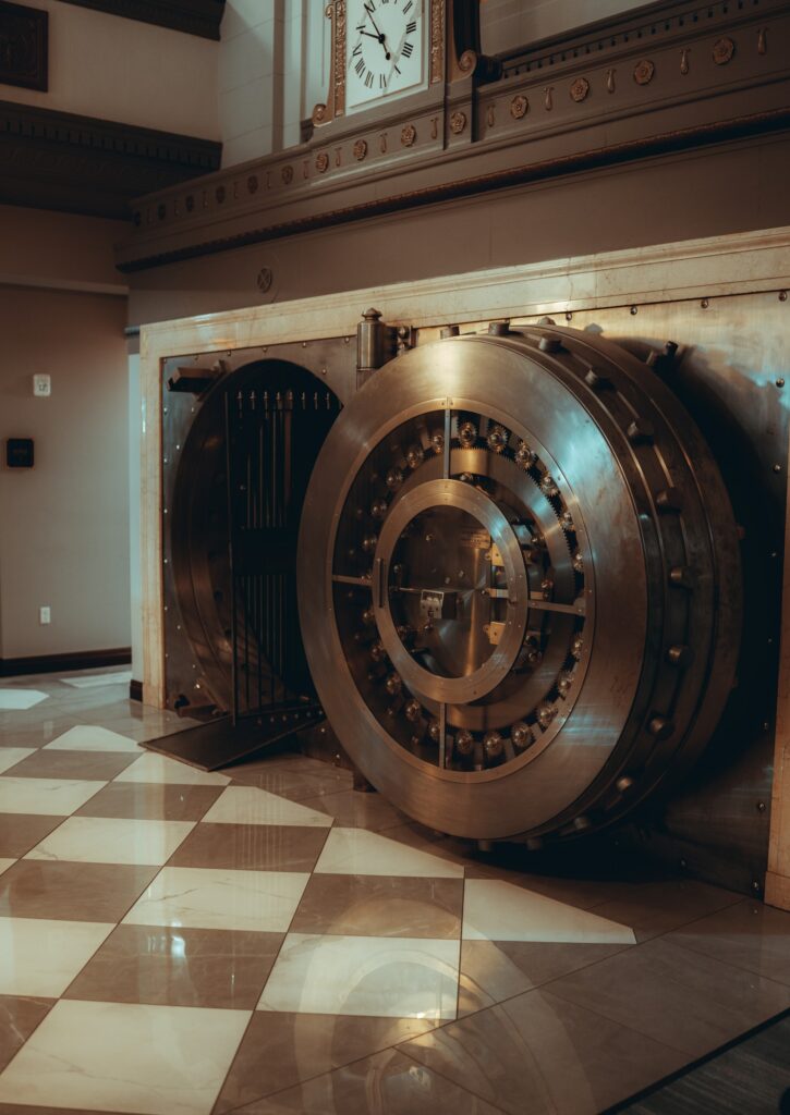 A large opened vault door inside of an lobby with marble checkered white and brown tiles