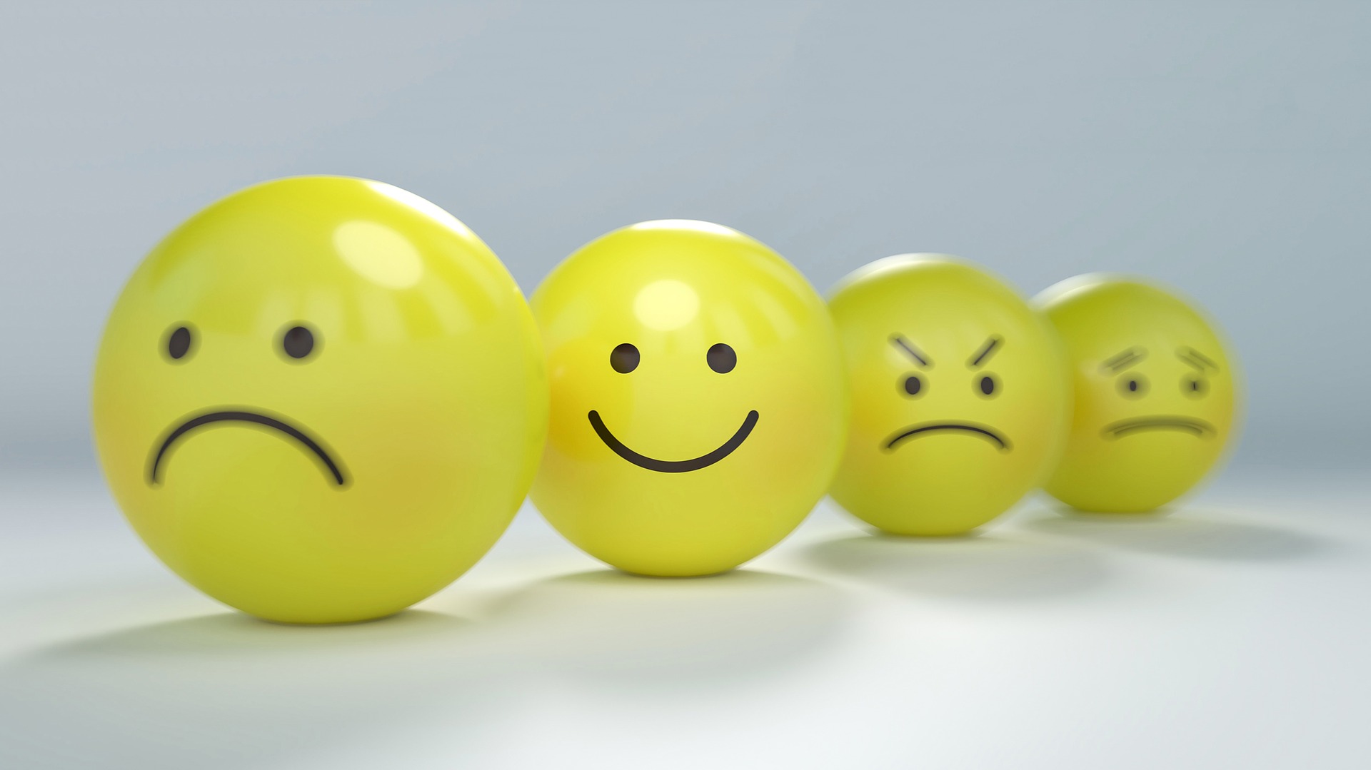 Four yellow smiley face balls in a row showing different emotions