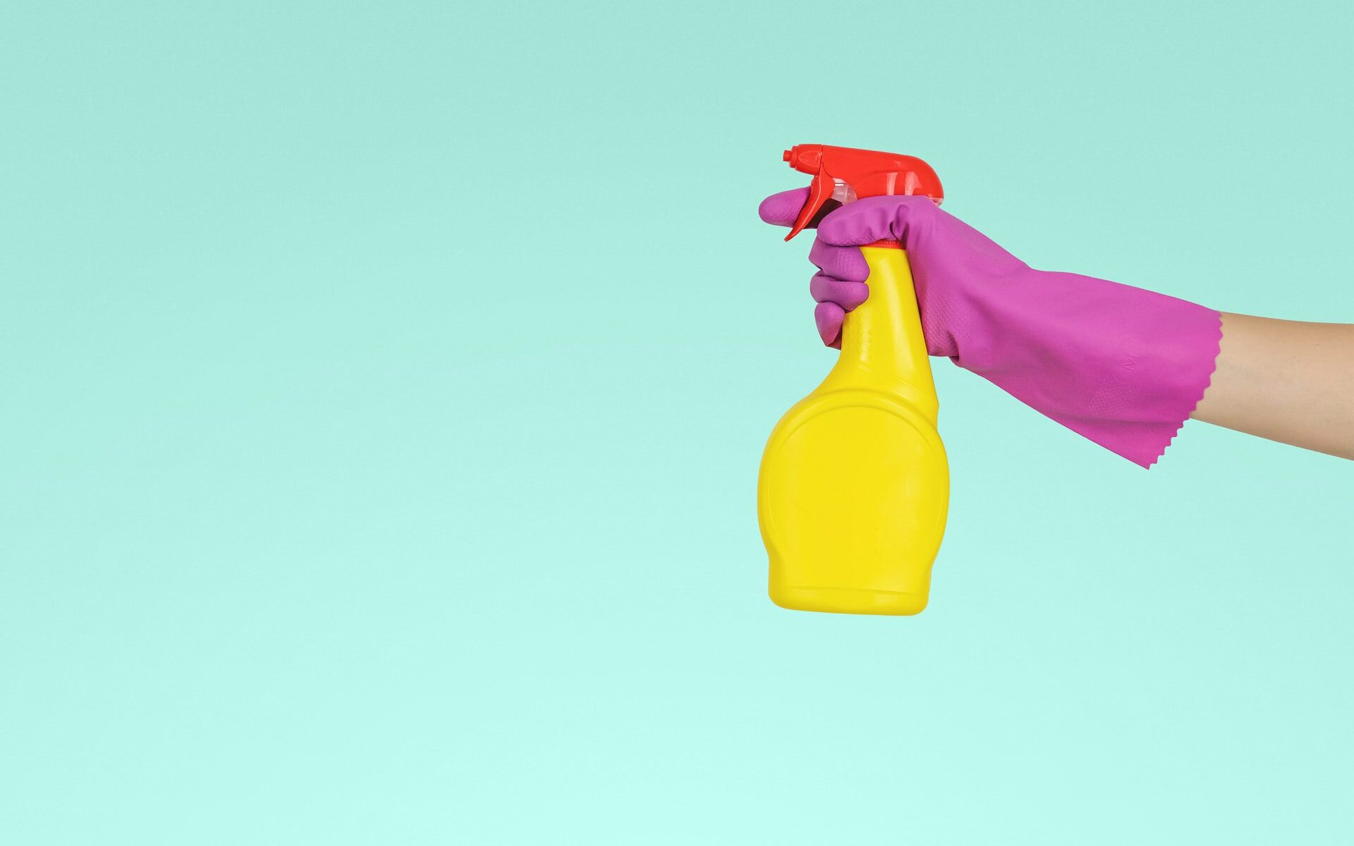 Aqua colored background with a hand wearing a magenta rubber glove, holding a yellow spray bottle