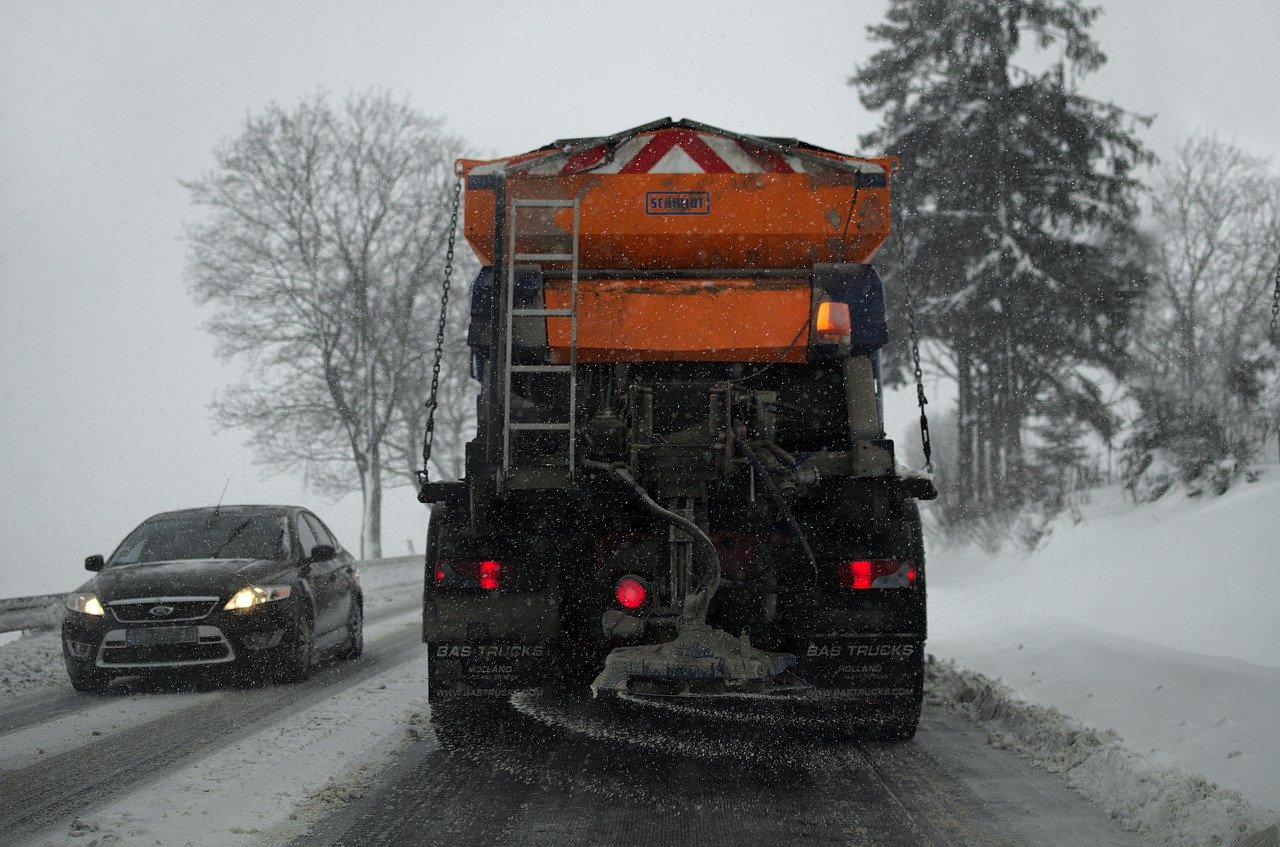 The back side of a snow plow spreading salt and sand on the road.